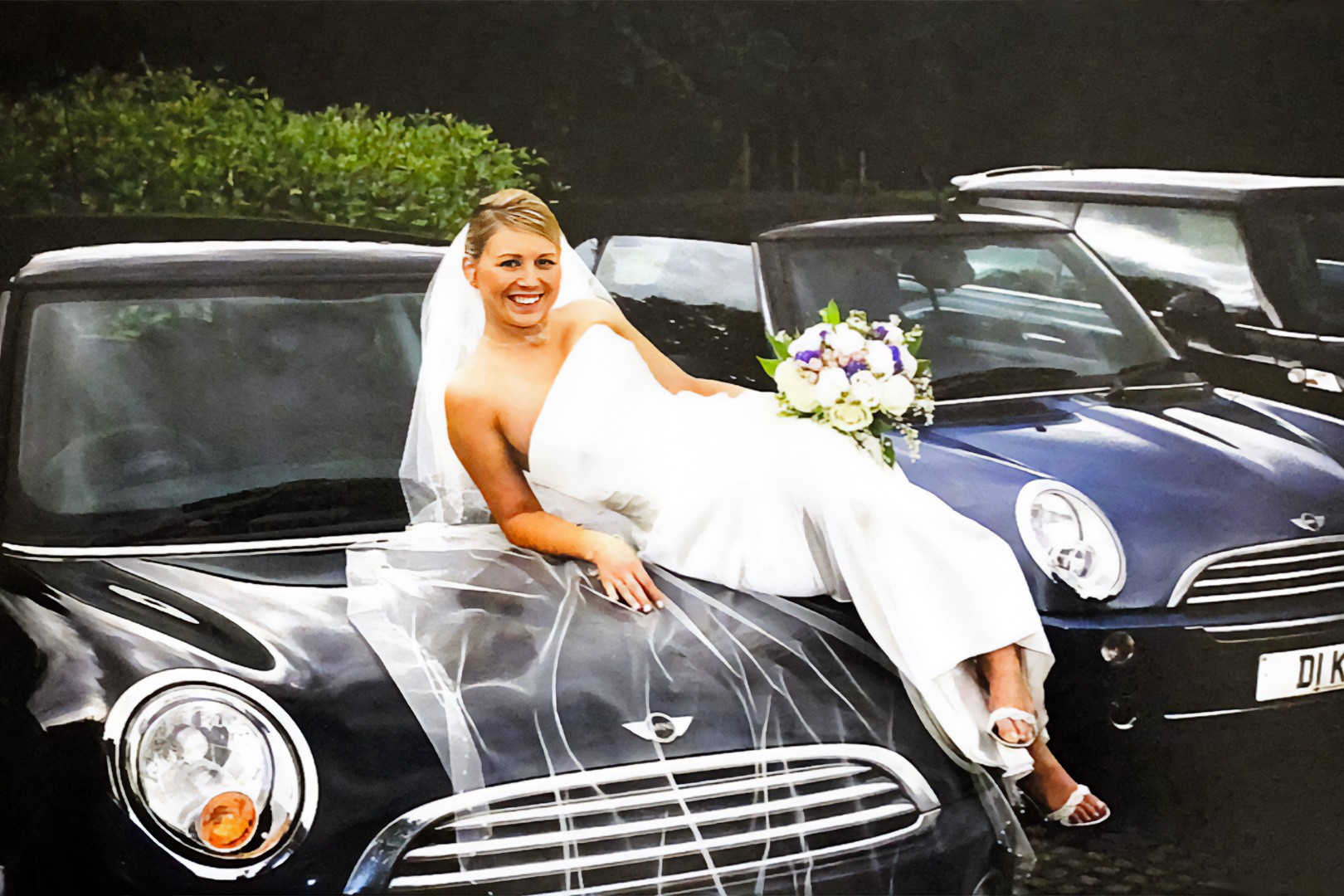 Bride sitting on the bonnet of a classic MINI holding a bouquet on her wedding day